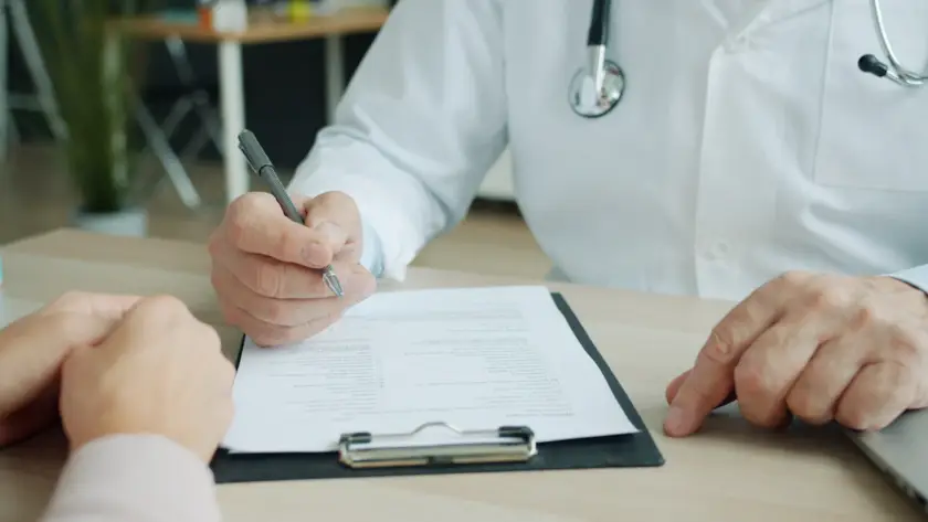Médico dermatologista escrevendo no prontuário durante consulta em Belo Horizonte